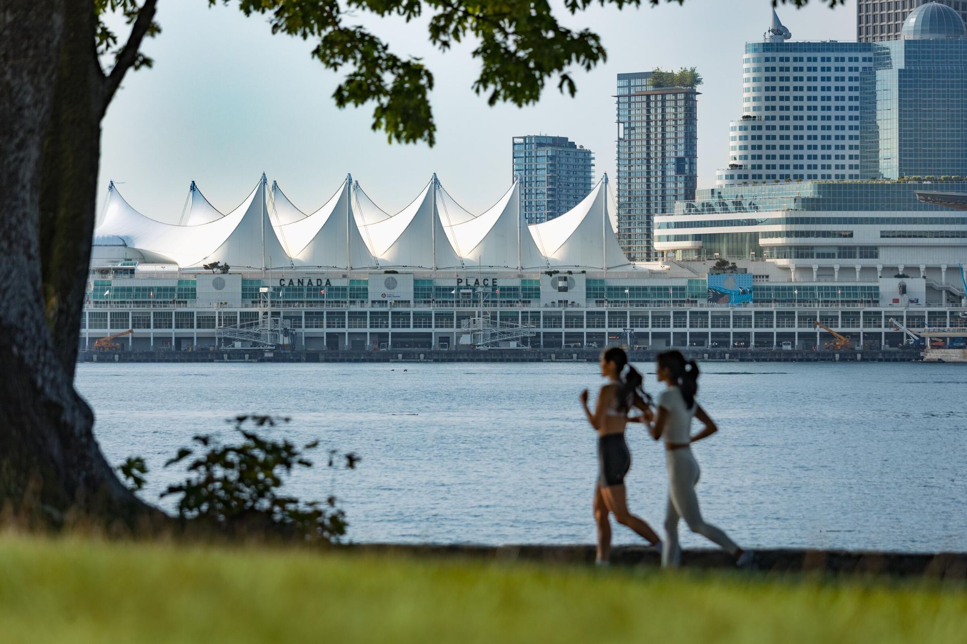 Canada Place and its white sails across the harbour, with two runners on the Stanley Park seawall in the foreground
